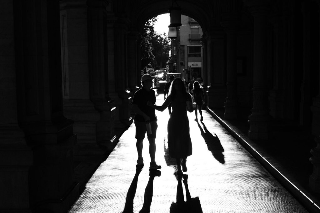 Silhouette of a couple walking in a sunlit city passageway, creating dramatic shadows.