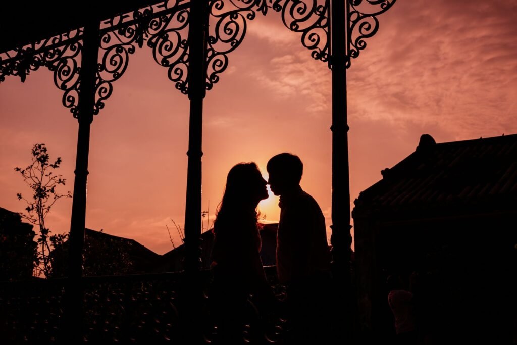 Silhouette of a couple sharing an intimate moment at sunset with ornate ironwork in the foreground.