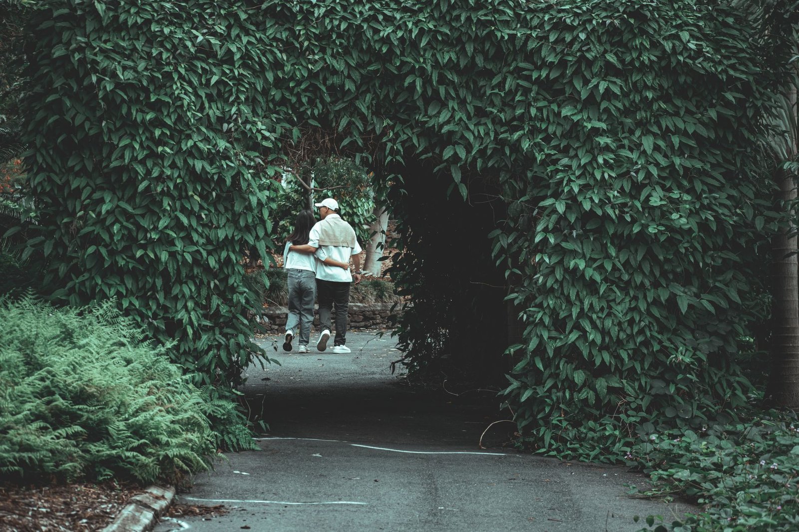 Scenic view of a couple walking through a leafy archway in a tranquil garden setting.