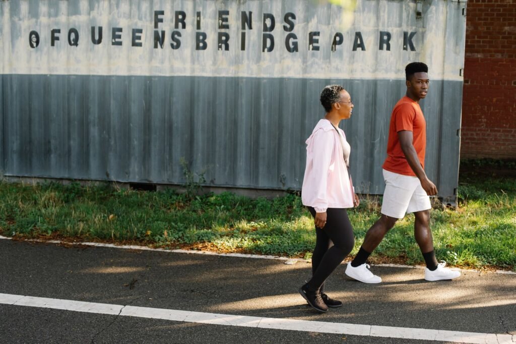 Two people walking in Queensbridge Park, enjoying a sunny outdoor stroll together.