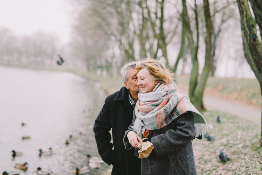 A senior couple walking by the lake, sharing a romantic moment in winter.