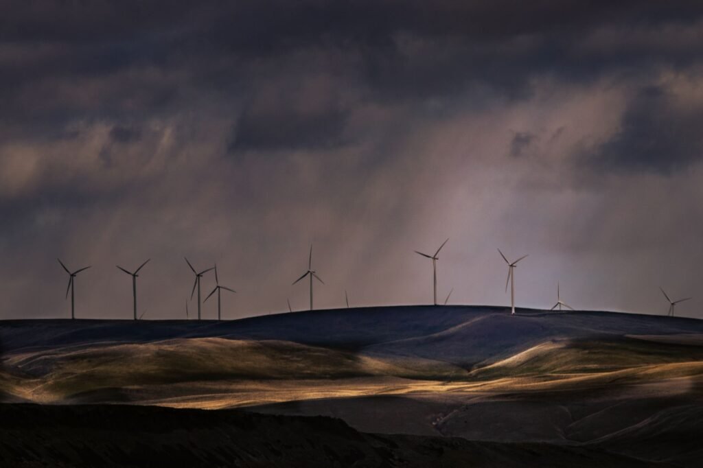 Dramatic landscape of a wind turbine farm on rolling hills with a moody sky.