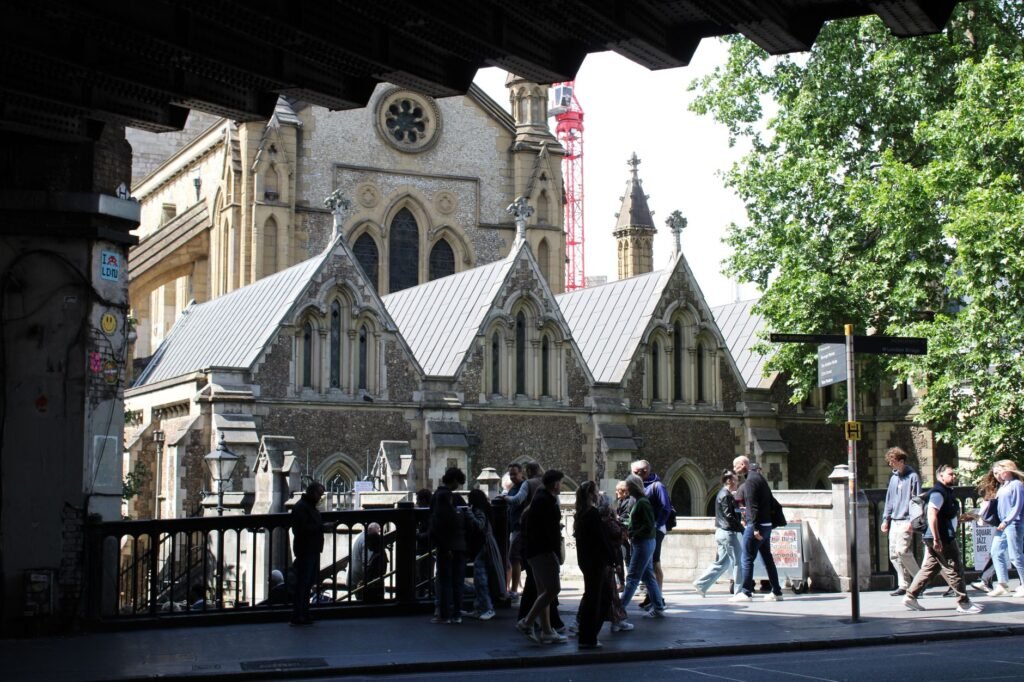 People walking near a historic church in a bustling city street under a bridge.