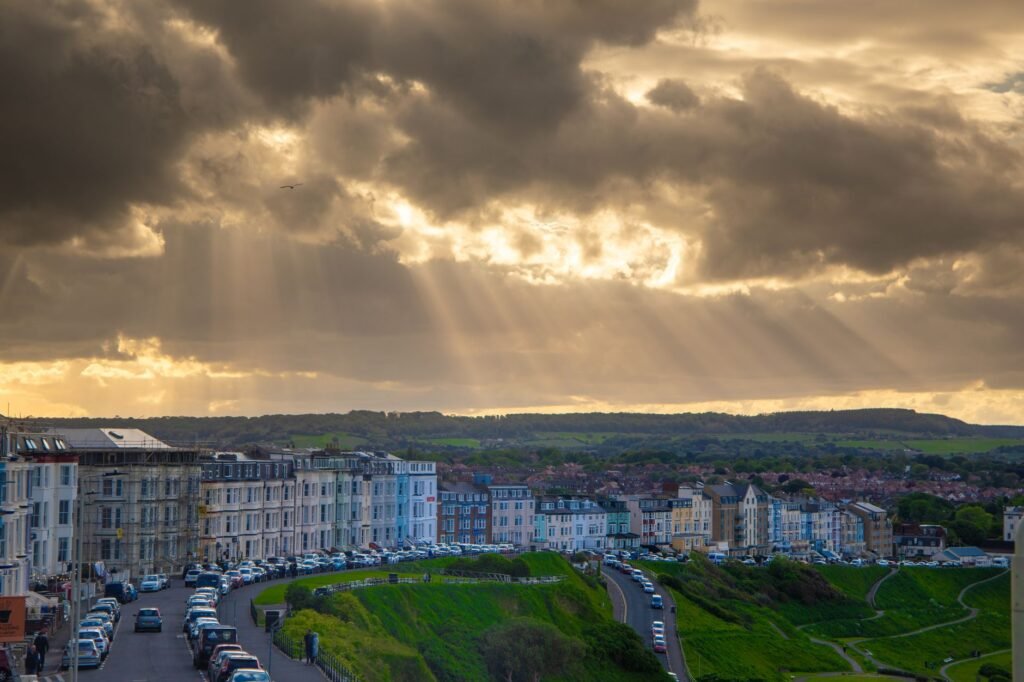 Sun rays pierce through dramatic clouds over a coastal cityscape with historic buildings.