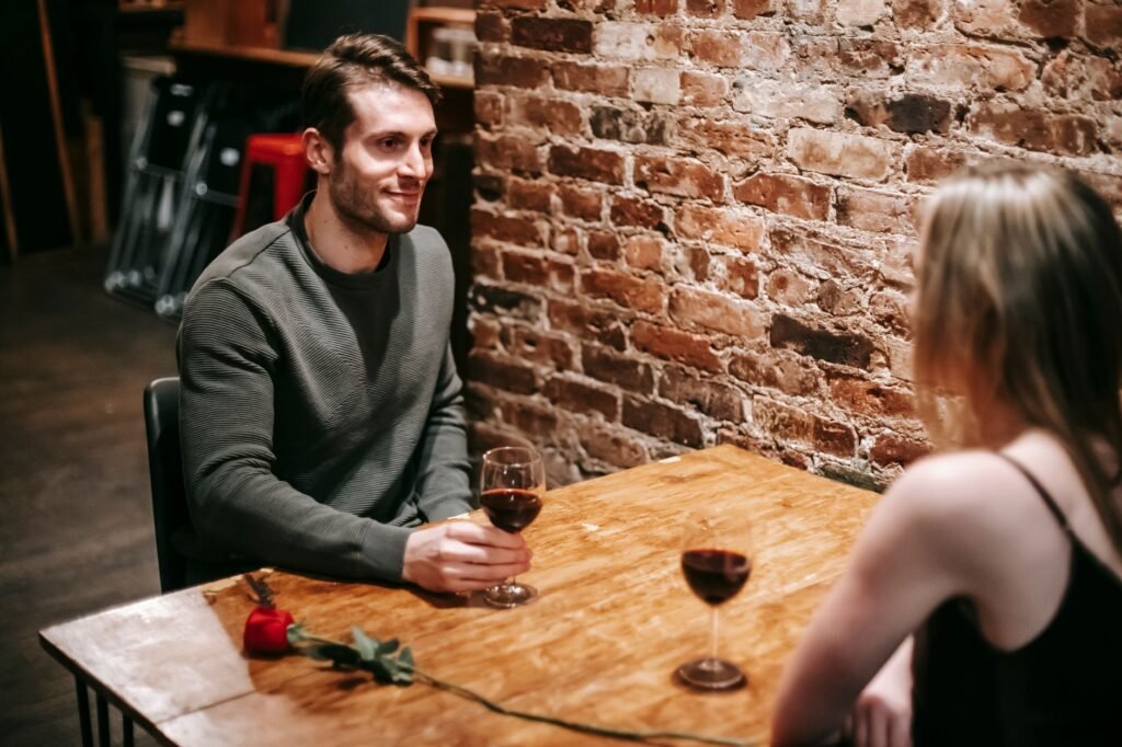 High angle of young happy couple sitting at wooden table and drinking red wine in cozy cafe