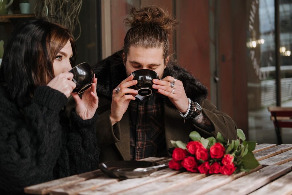 Young man with closed eyes drinking hot beverage near girlfriend while resting at cafeteria table with blooming flowers