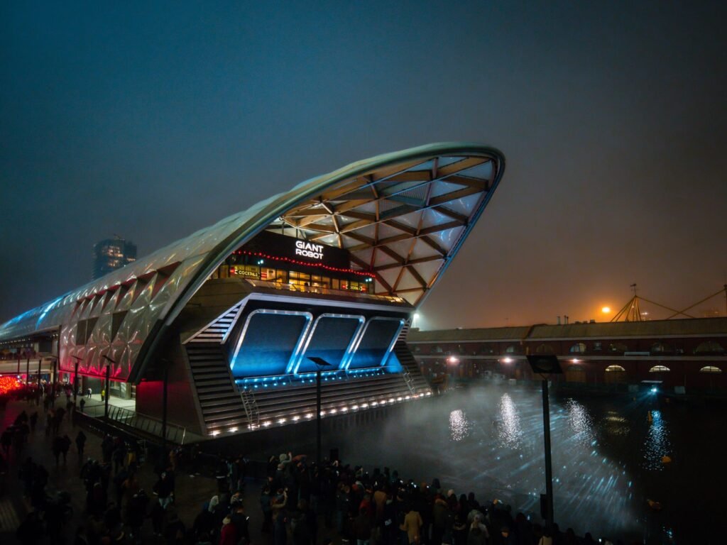Illuminated Canary Wharf station with reflections on water during a bustling evening in London.
