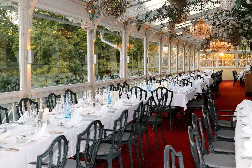 Elegant restaurant interior with formal place settings and chandeliers in a sunny conservatory.