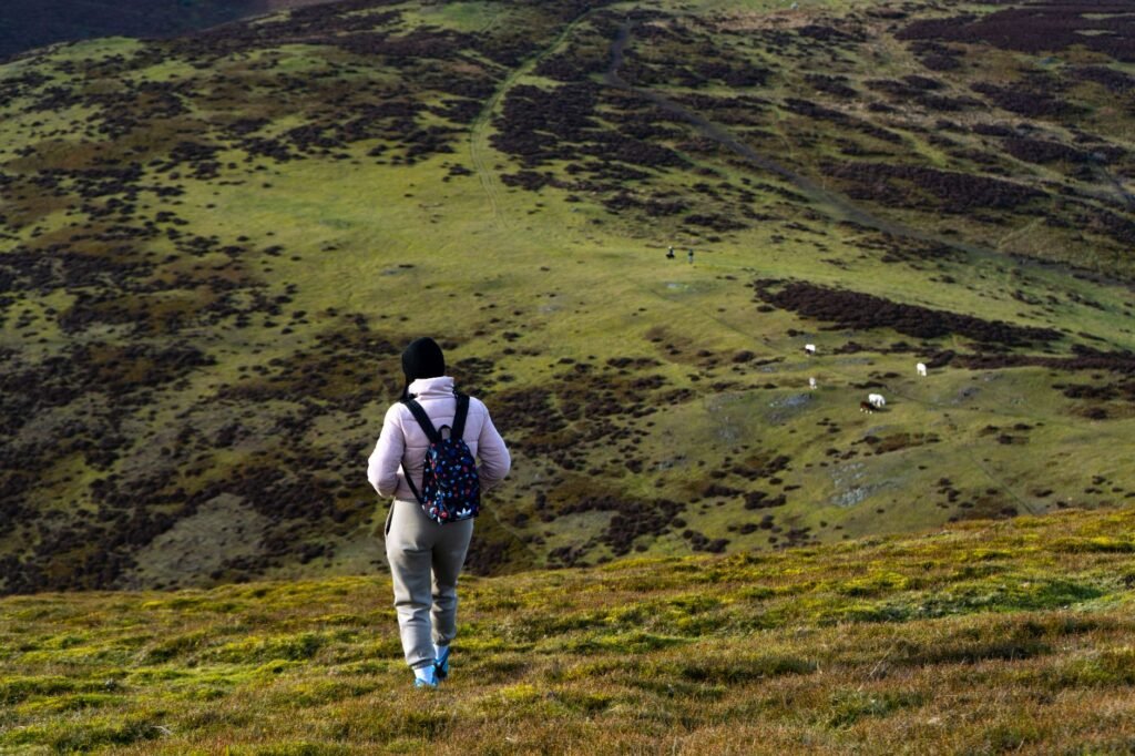 A lone hiker with a backpack explores a vast, open landscape of rolling hills.