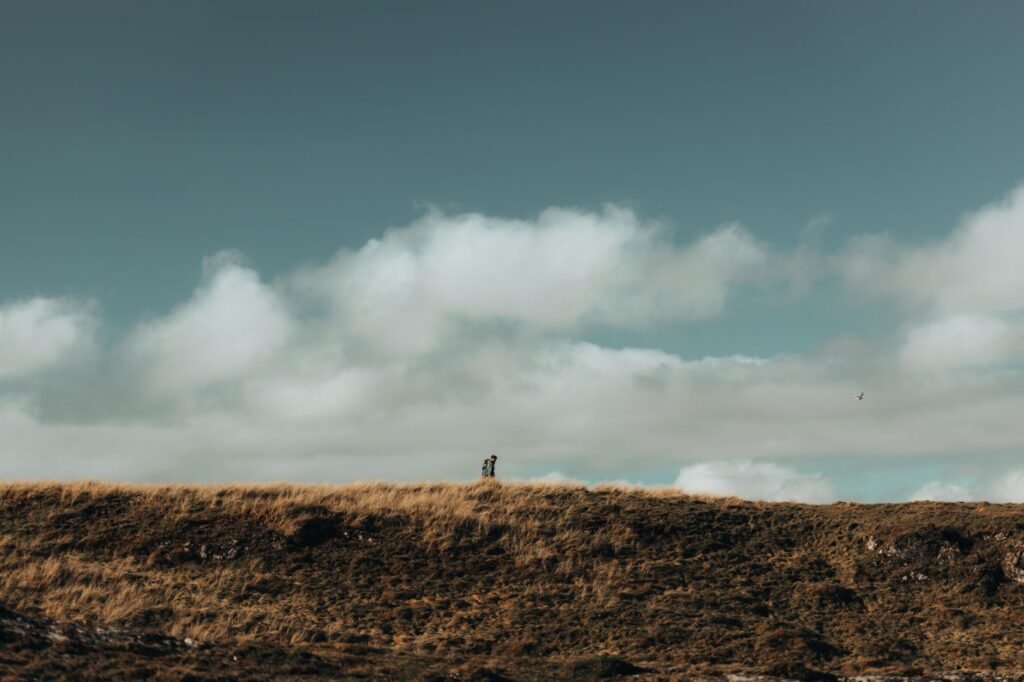 A scenic view of a person walking on a hill under dramatic clouds and a clear sky.