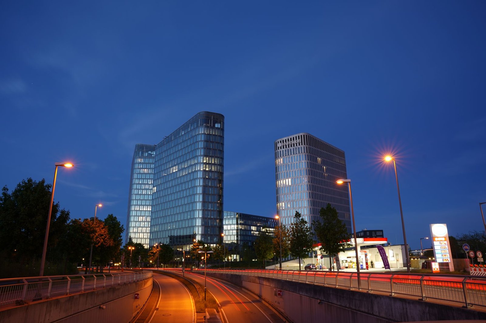 A modern Munich cityscape with illuminated skyscrapers at dusk under a clear blue sky.