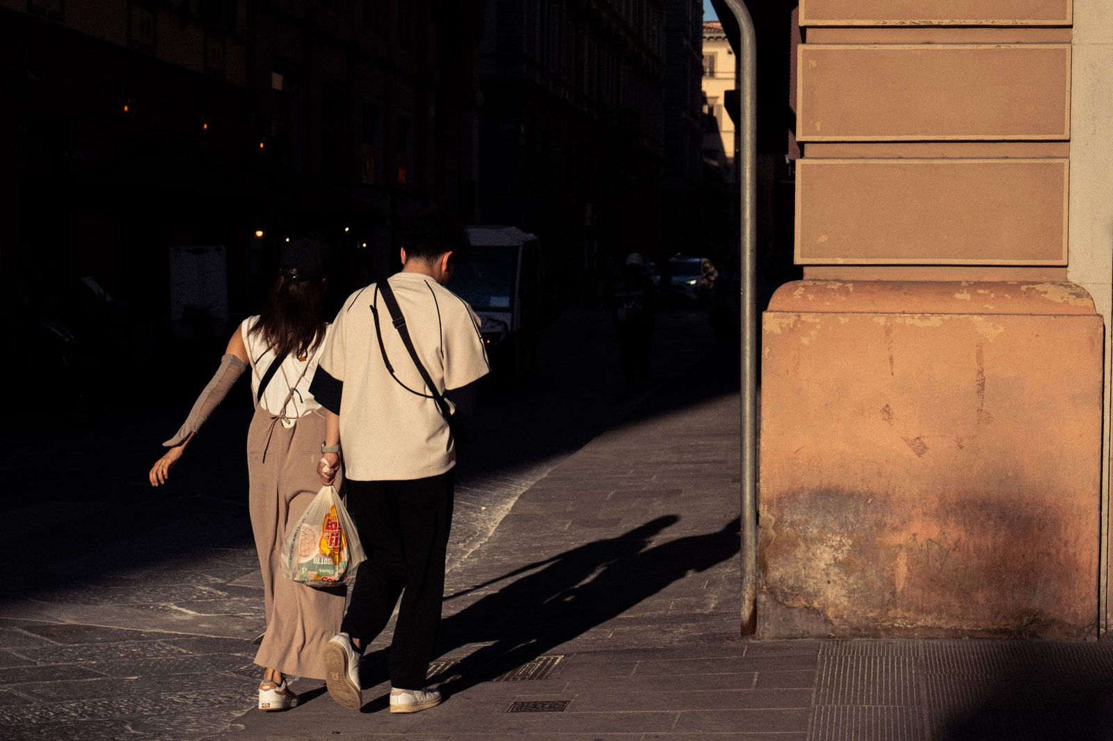 A couple walking in Florence during the evening, casting long shadows on a sunlit street.