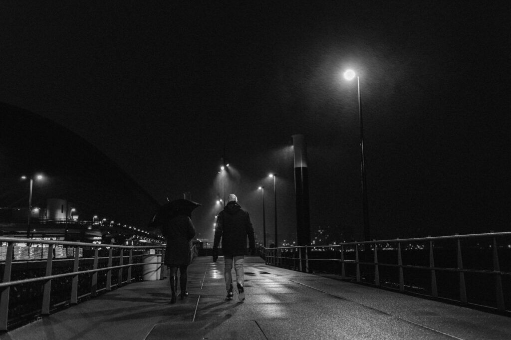 A couple walking on a dimly lit Amsterdam street at night under street lamps.