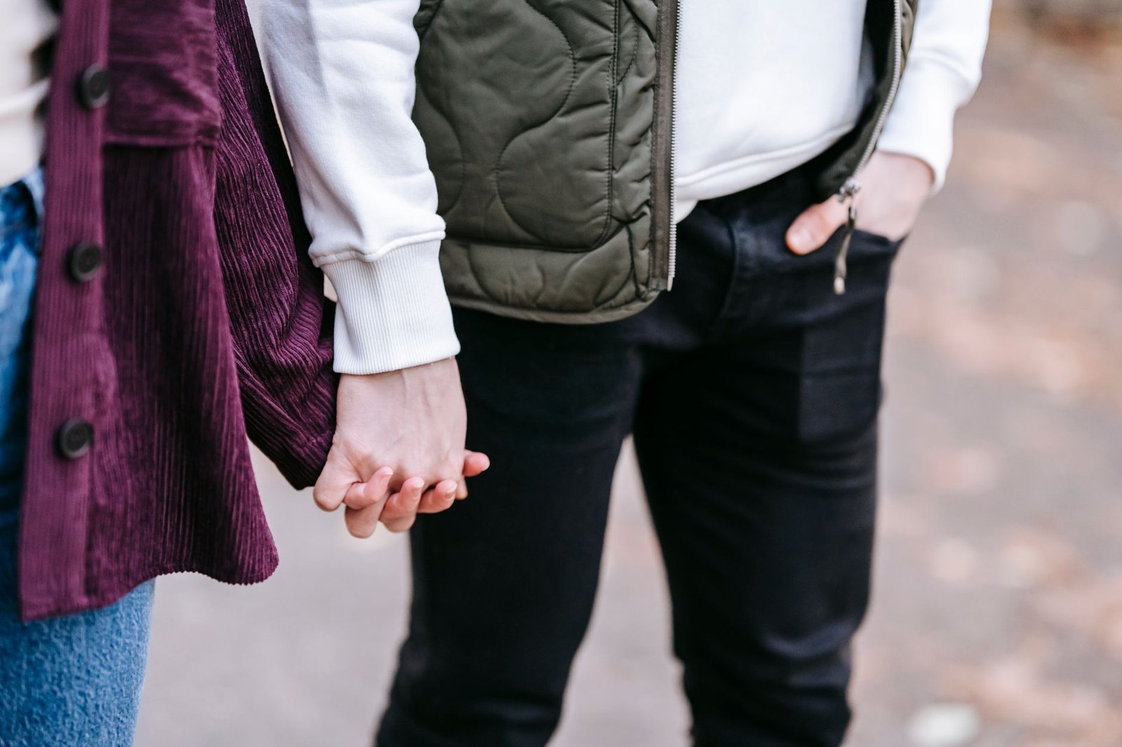 Crop anonymous couple touching hands and walking on blurred background of urban park