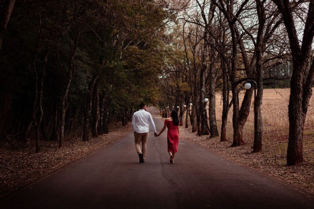 A romantic couple walking hand in hand down a tree-lined path in Maringá, Brazil.