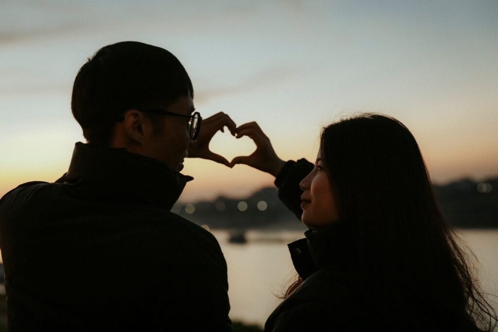 Silhouette of a couple forming a heart shape with hands at sunset, capturing romantic ambiance.