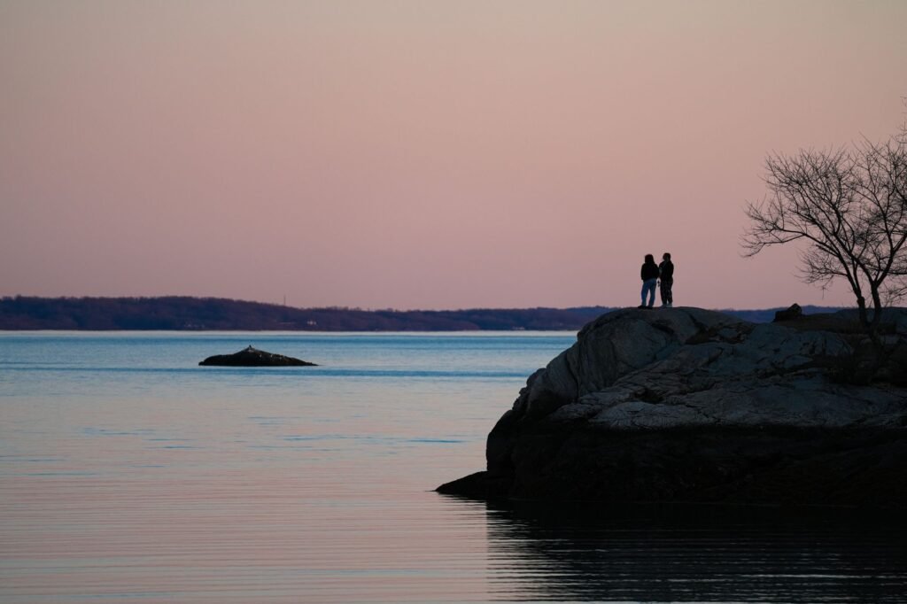 Silhouetted couple standing on a rock at Cove Island Park during sunset, showcasing a pink sky over Stamford, Connecticut.