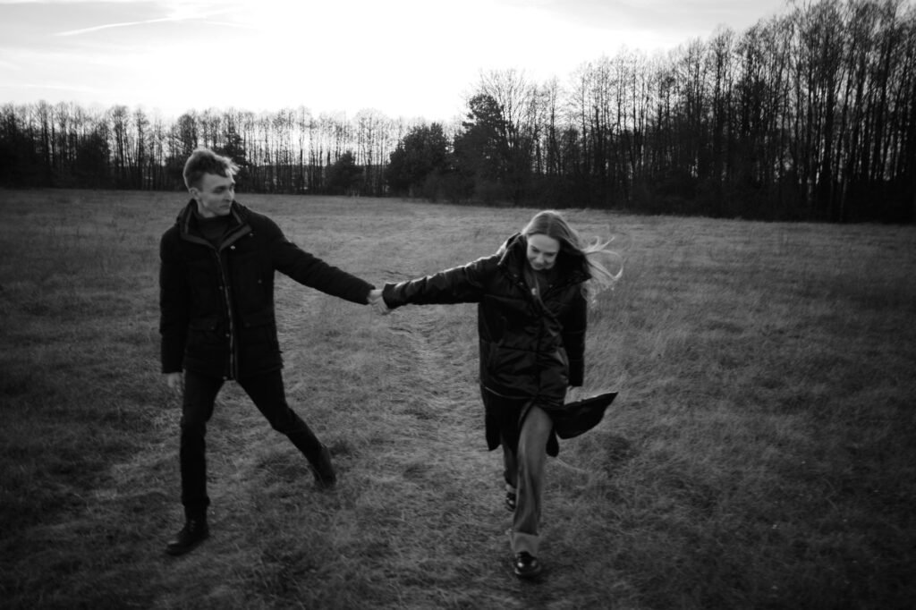 A couple walking hand in hand through a grassy field in black and white, exuding romance.
