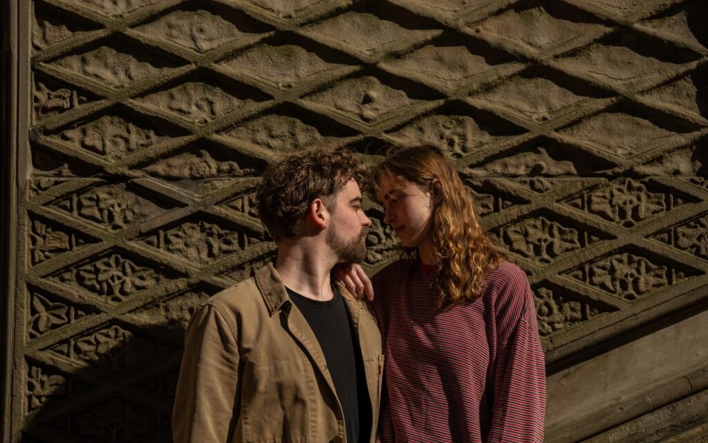 A couple shares a tender moment by a detailed stone wall during a sunny day in Central Park, NYC.