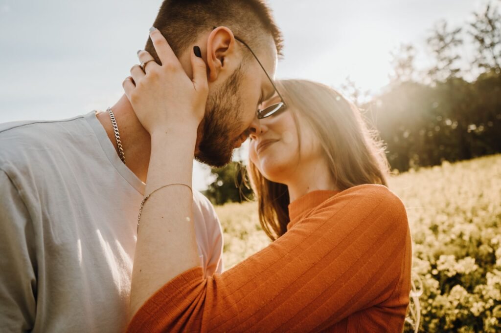 Young couple shares a romantic moment in a sunlit field, showcasing love and affection.