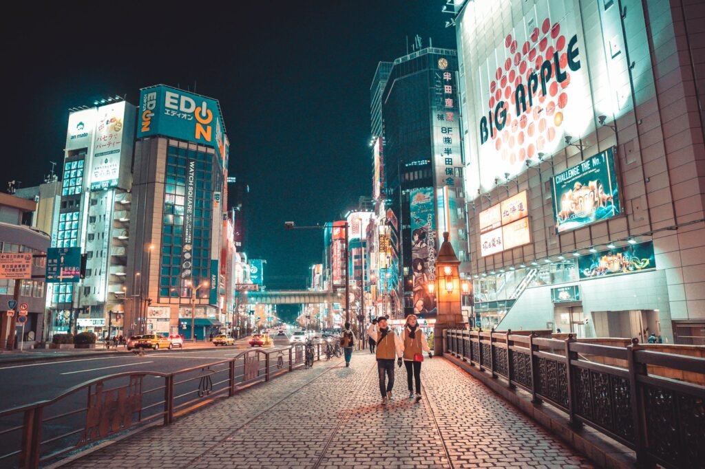 Urban Japan cityscape at night with illuminated buildings and people walking along the street.