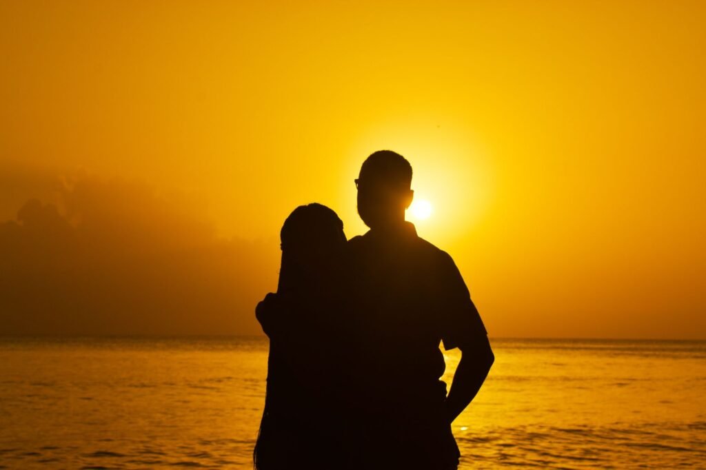 A romantic silhouette of a couple embracing at sunset with a stunning ocean backdrop.