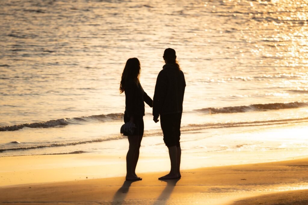 Silhouette of a couple holding hands by the sea at sunset, creating a serene and romantic atmosphere.
