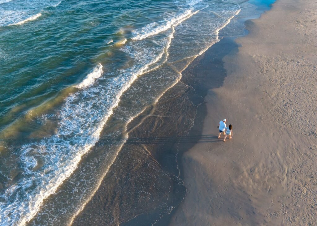A couple enjoys a romantic beach walk along Corpus Christi's shoreline during a serene sunset.