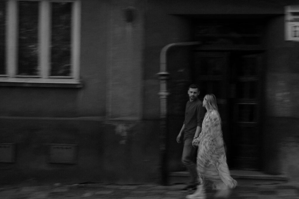Blurry image of a couple holding hands while walking on the sidewalk in a monochrome setting.