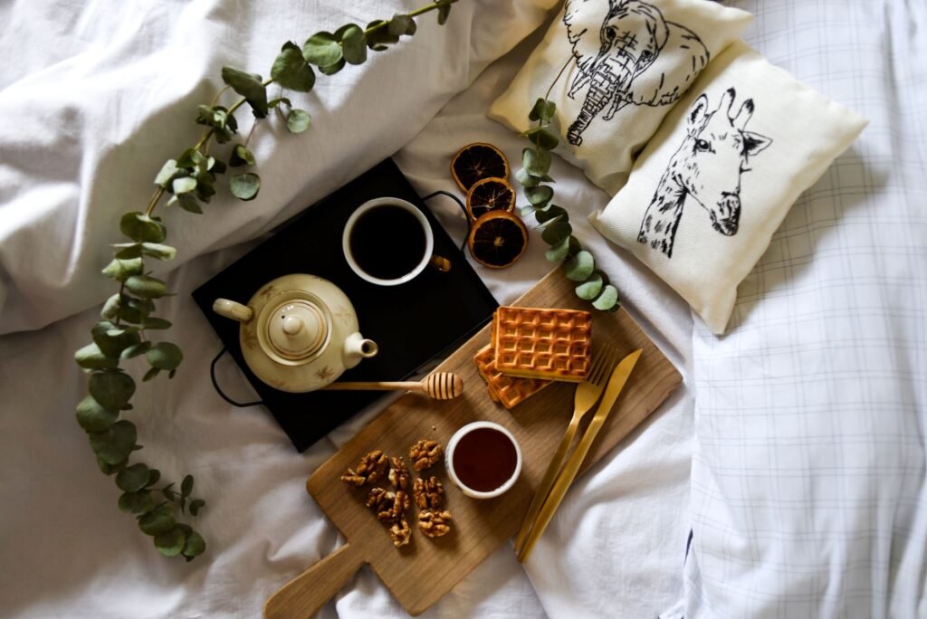 Cozy breakfast in bed with tea, waffles, walnuts, and honey on a tray, surrounded by greenery.