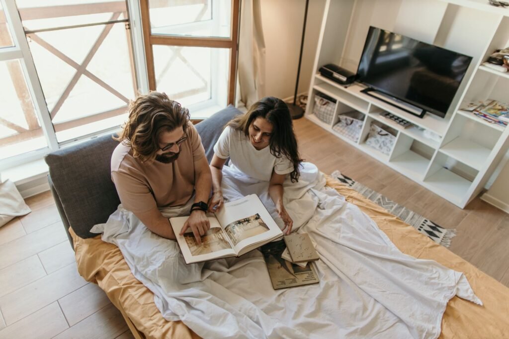 A couple enjoys reading together in a cozy, well-lit bedroom setting.