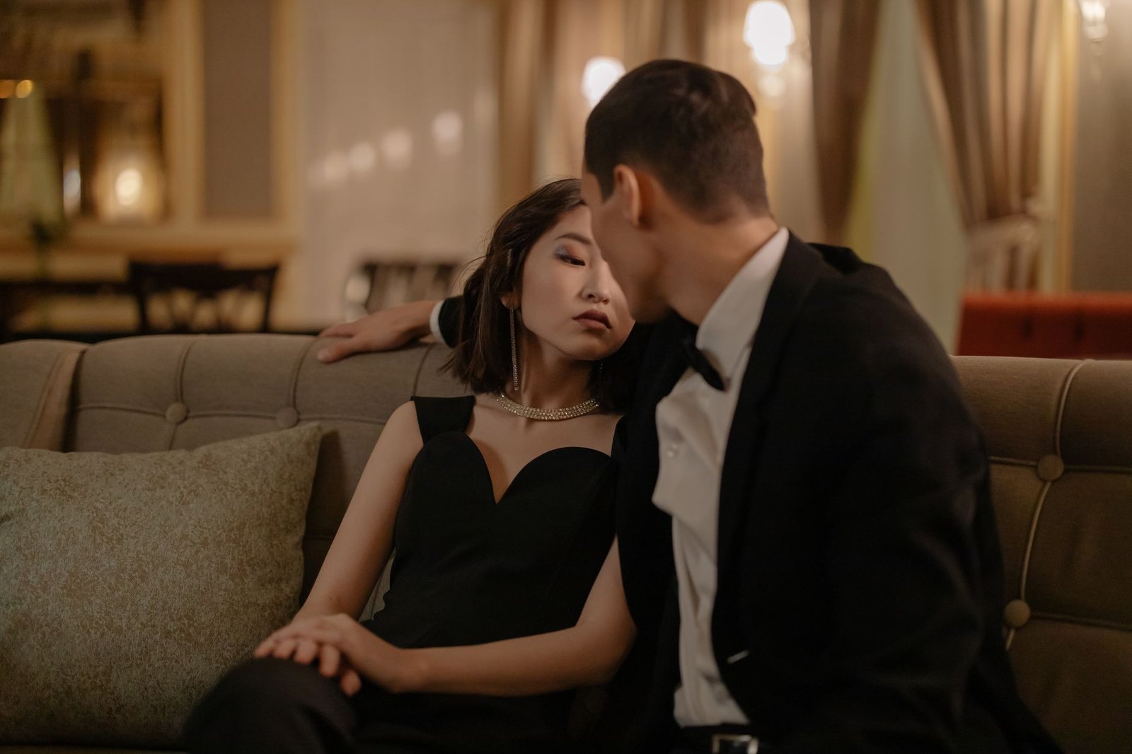 A stylish couple in formal attire sharing a romantic moment indoors, evoking luxury and affection.