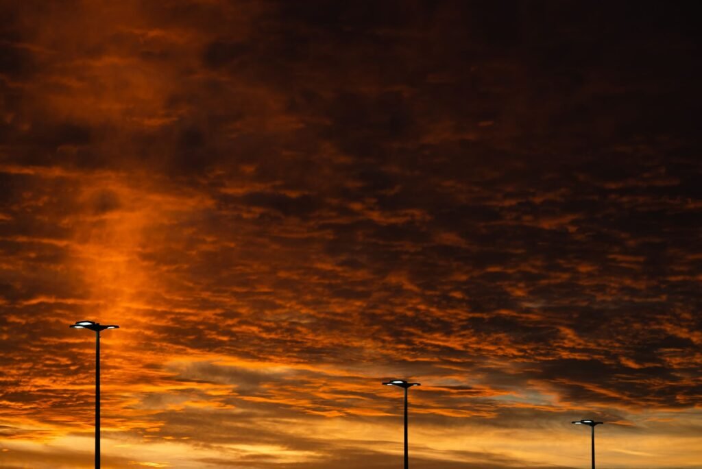 Vivid sunset sky with street lamps silhouetted against a rich orange hue, creating a dramatic scene.
