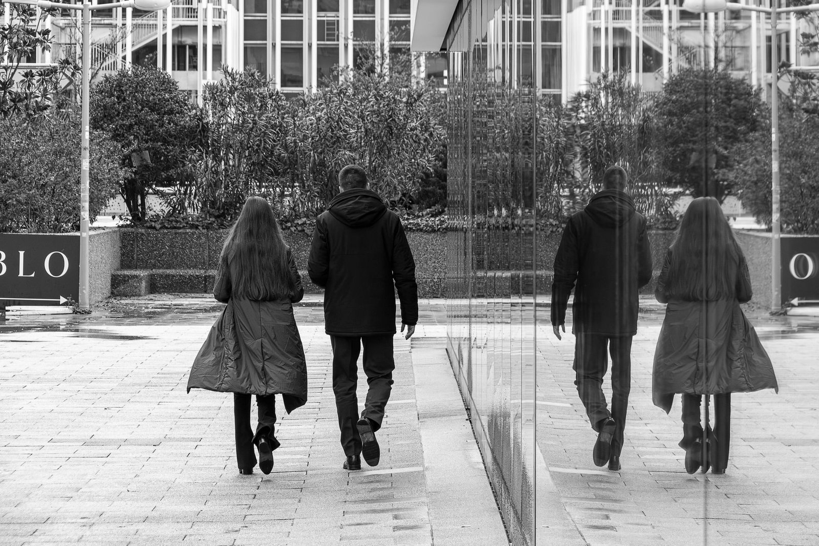 A black and white photo of two people walking by a reflective surface in Madrid.
