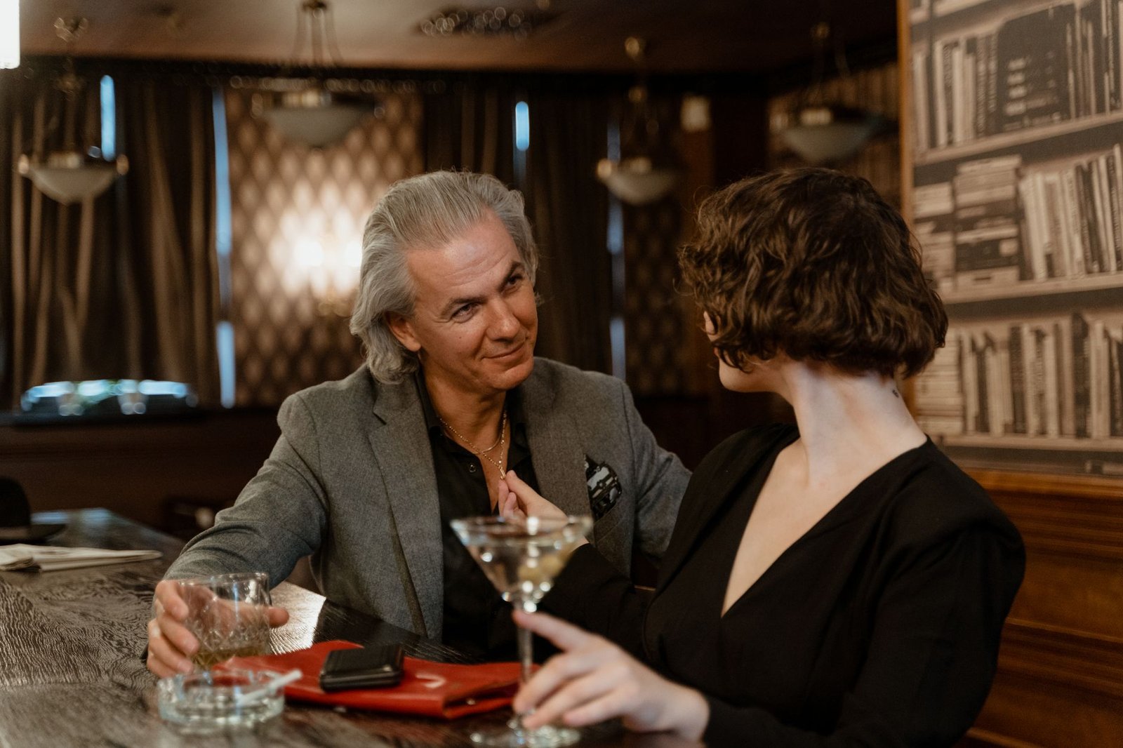 Two adults enjoying drinks and conversation in a stylish bar, surrounded by cozy decor.