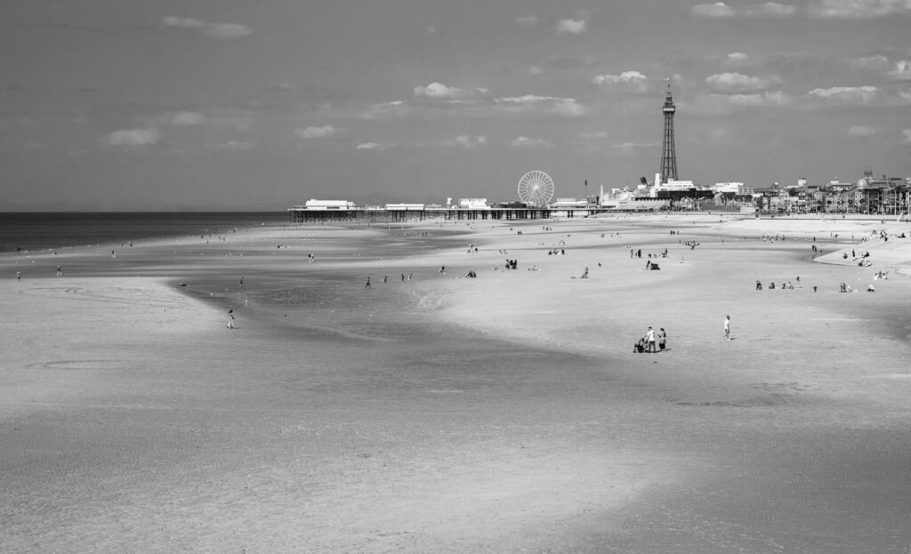 Blackpool beach with iconic tower and Ferris wheel in black and white, scenic view.