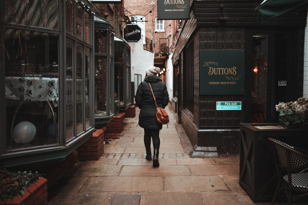 A lone woman walks through a quaint urban alley lined with shops, creating a cozy atmosphere.