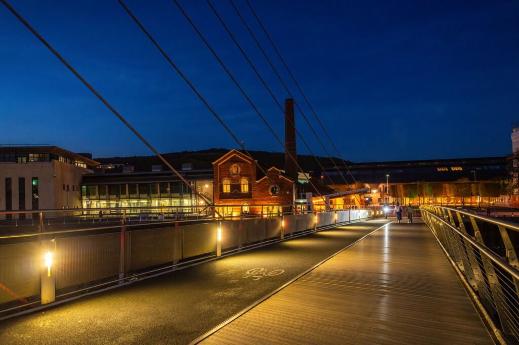 A modern bridge illuminated at night with buildings in warm light, showcasing urban architecture.