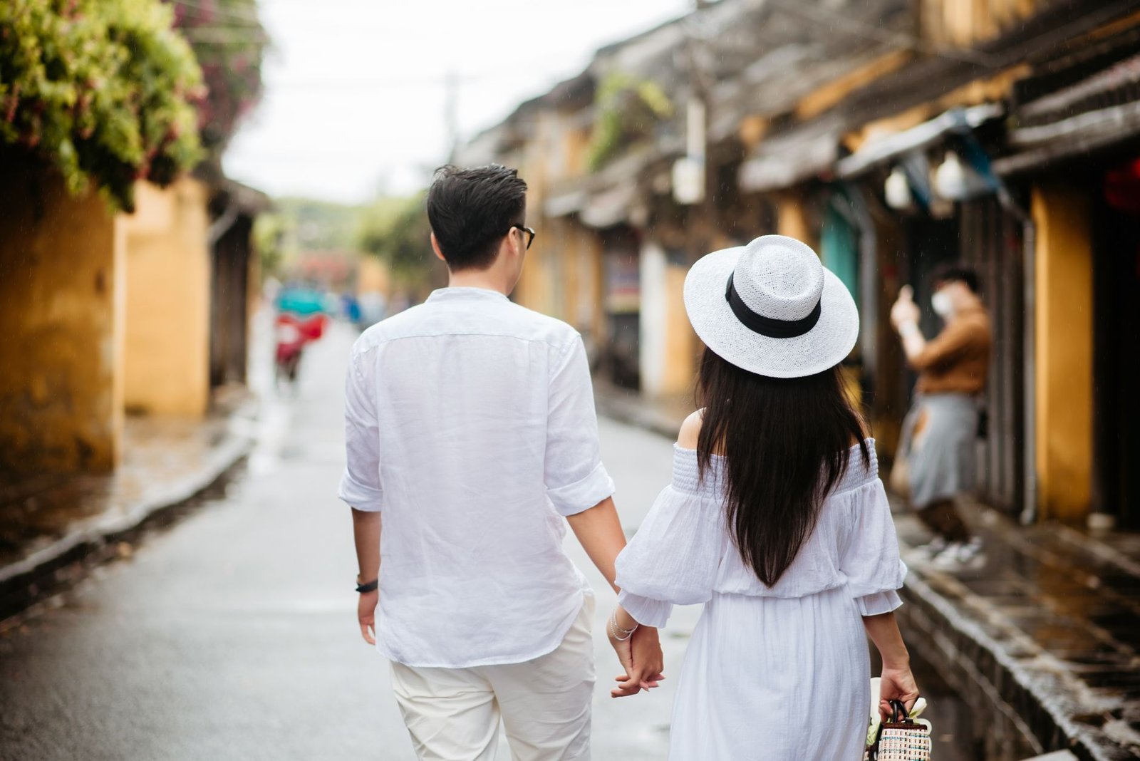 A couple holding hands walking down a charming street in summer, wearing white clothes.