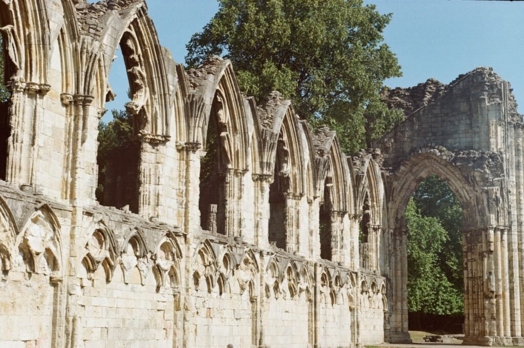 Historic stone arches of St Mary's Abbey ruins captured in York, England with lush greenery around.