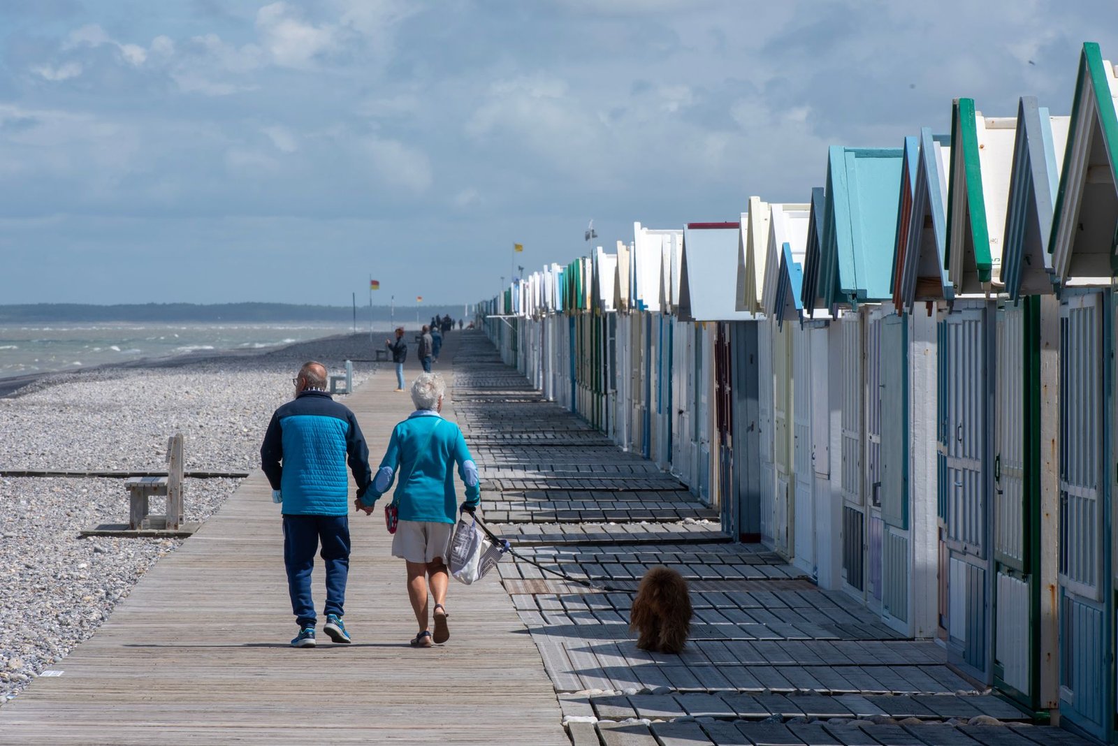 Elderly couple walking along beach huts on Cayeux-sur-Mer boardwalk, France.