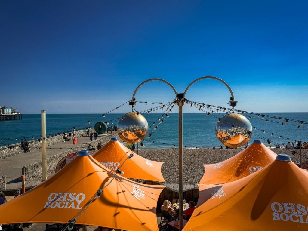 Explore the vibrant seaside cafe scene in Brighton with iconic orange umbrellas and a stunning coastal view.