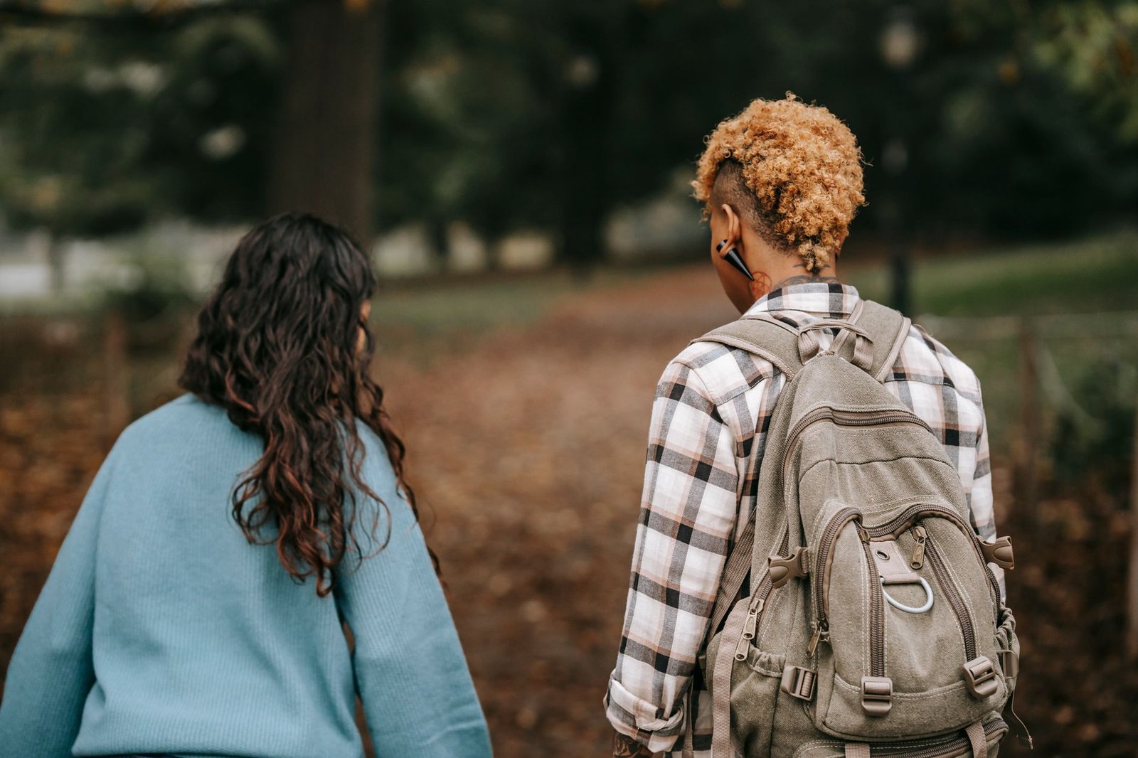Back view of unrecognizable female friends in casual outfits strolling in park together and talking