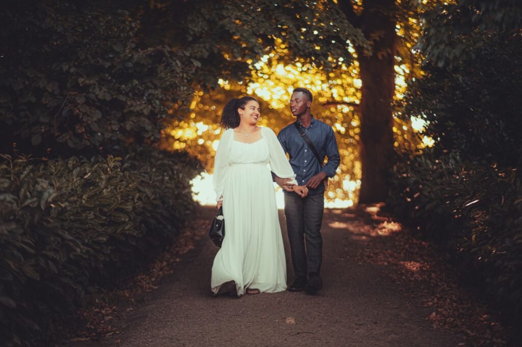 Couple strolling hand in hand on a sunlit forest path surrounded by lush greenery.