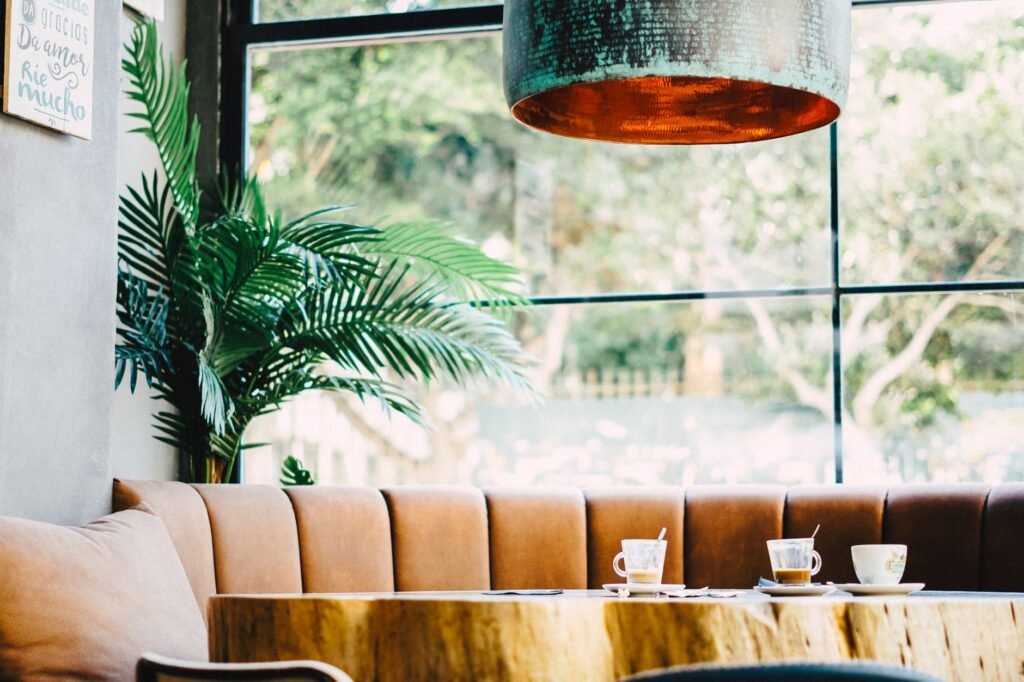 Inviting café interior with a brown sofa, vibrant plant, and coffee cups on a wooden table.