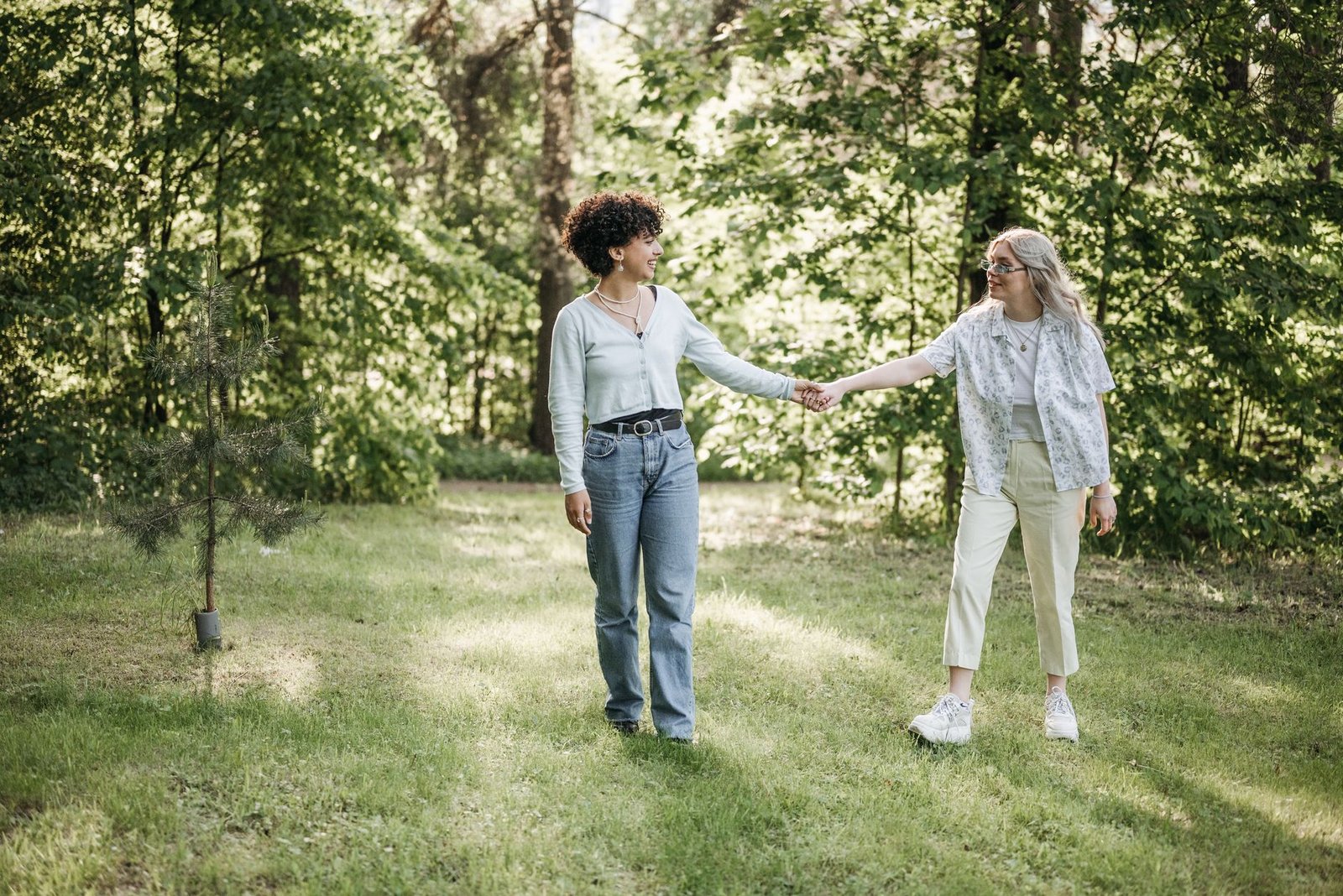 A lesbian couple holding hands and enjoying a walk in a sunlit green park.