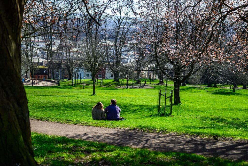 Two people enjoy a sunny spring day in a lush green park with blooming trees.