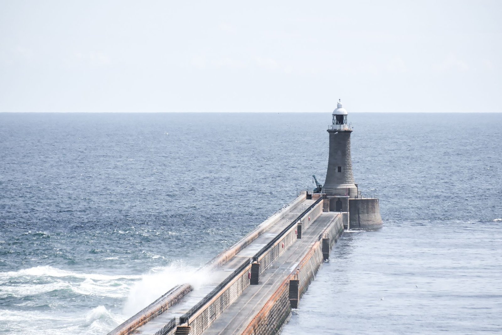 A serene view of a lighthouse guiding ships over the open sea with waves crashing on the jetty.