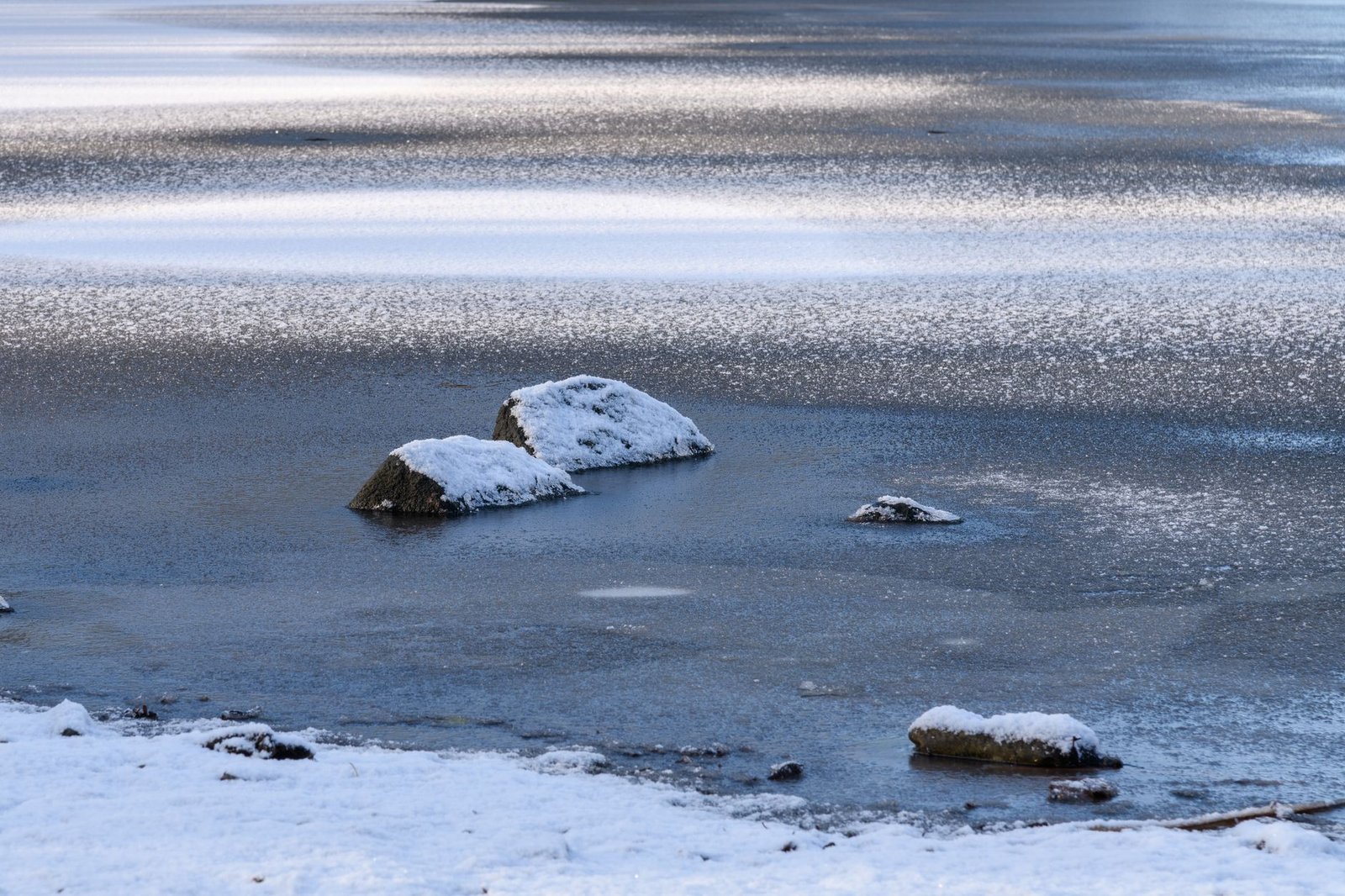 Frozen lake with snow-covered rocks, capturing the tranquil beauty of a winter landscape.