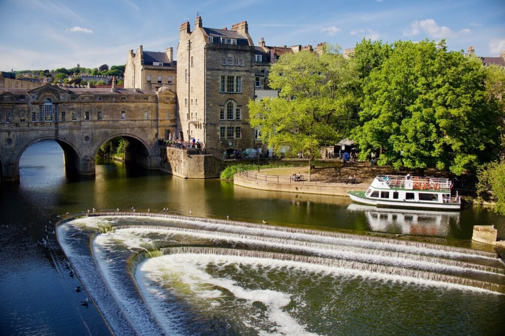 Scenic view of Pulteney Bridge over River Avon with a tour boat and waterfalls.